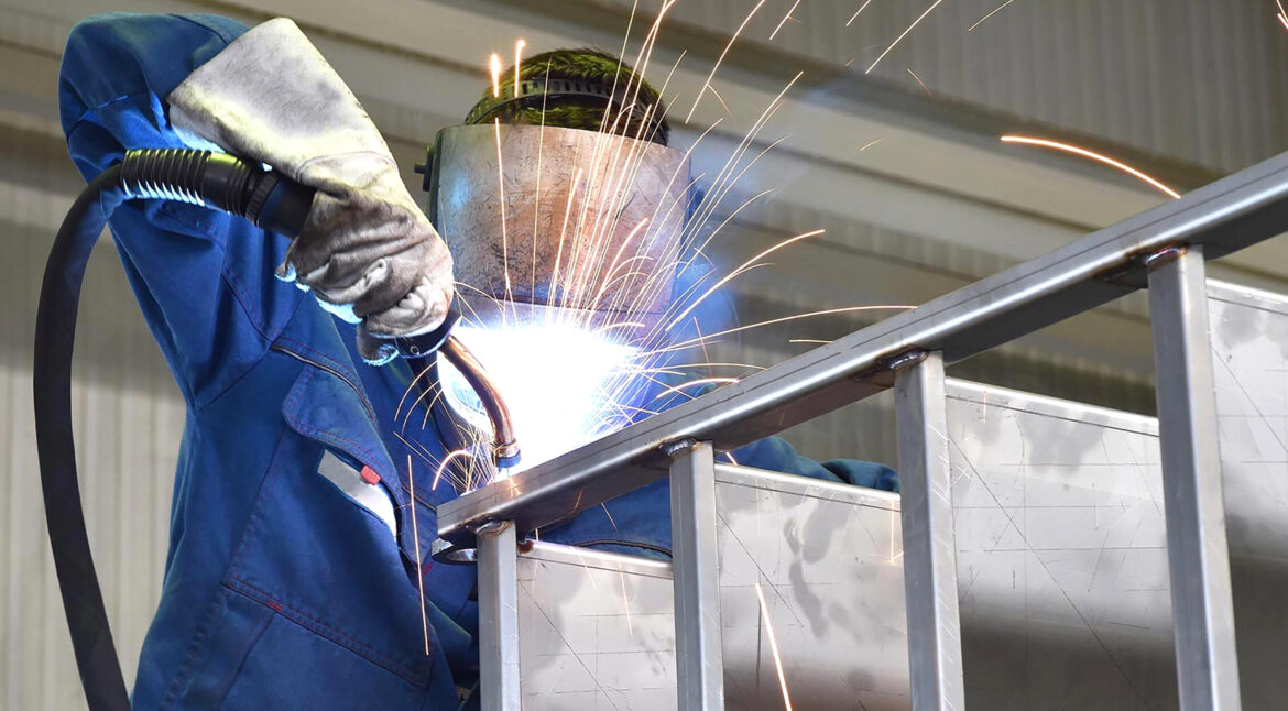Portrait of factory worker in protective equipment holding thumbs up in production hall.