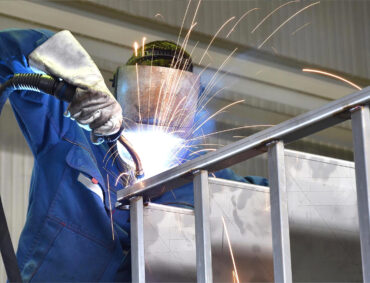Portrait of factory worker in protective equipment holding thumbs up in production hall.