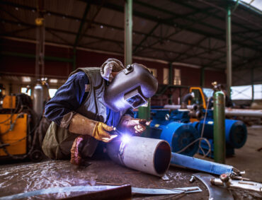 Industry male worker in protective uniform repairing metal pipe.