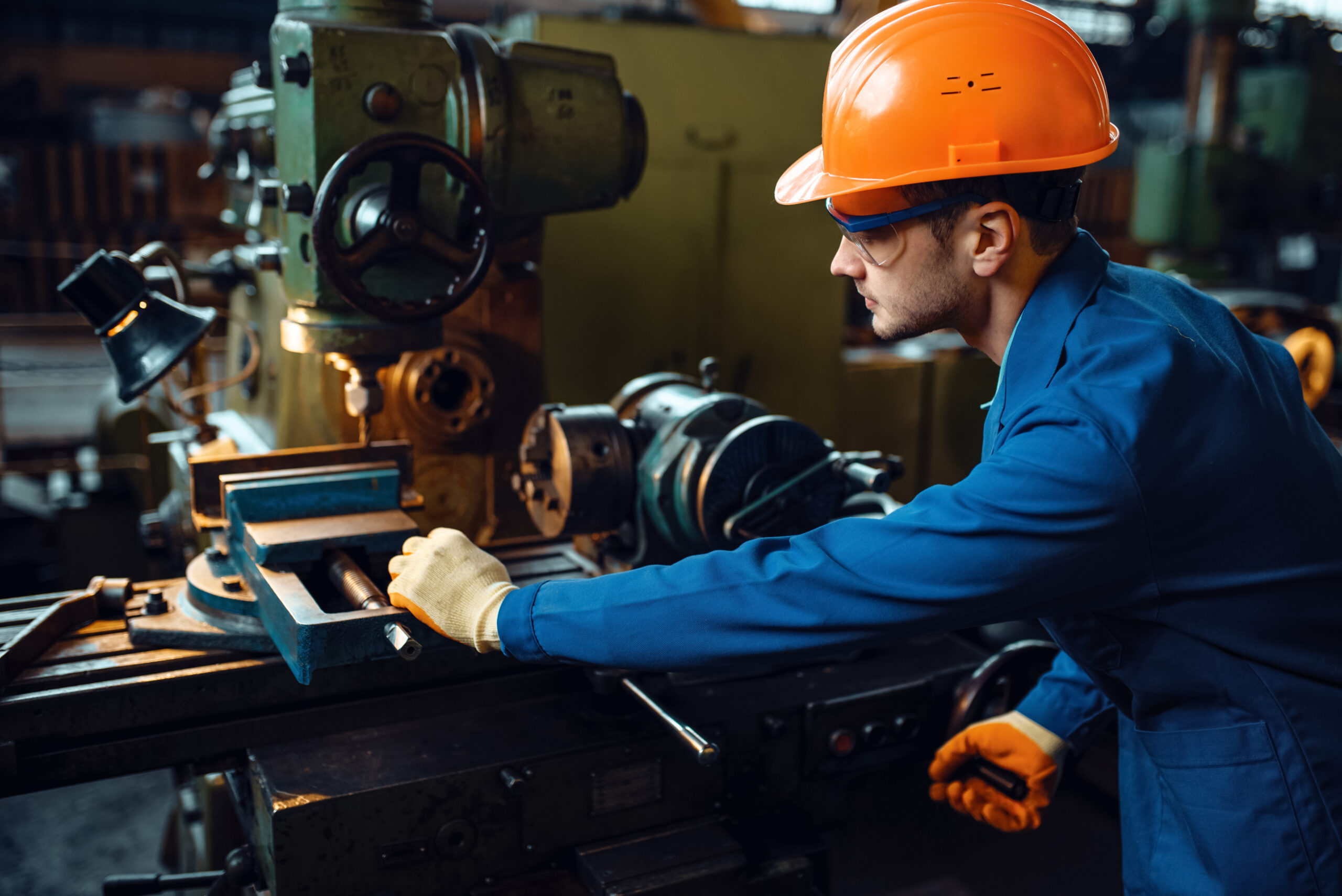 Worker in uniform and helmet works on lathe, plant. Industrial production, metalwork engineering, power machines manufacturing